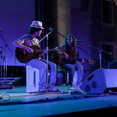 Concerto acustico con duo di chitarristi e percussioni su palco illuminato in blu
