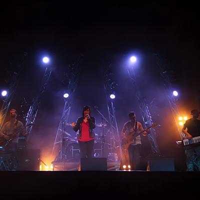 Band live su palco con scenografia truss e luci blu-viola durante esibizione musicale