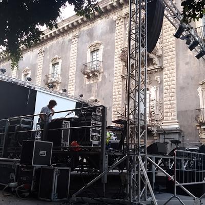 Montaggio impianto audio e luci su palco tecnico all’aperto davanti edificio storico