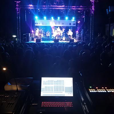 Concerto serale con palco illuminato, pubblico numeroso e regia audio luci in primo piano