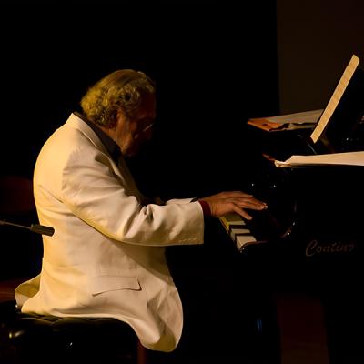 Pianista in abito bianco durante esibizione dal vivo su palco illuminato professionalmente