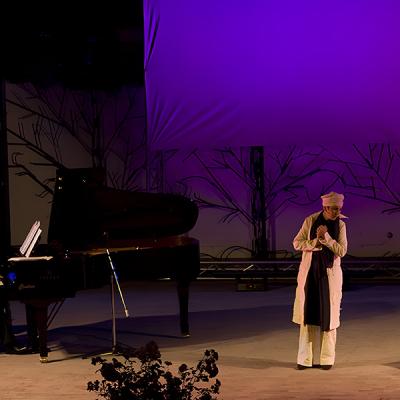 Esibizione dal vivo con pianista e attore su palco con fondale illuminato in viola