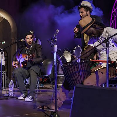 Concerto acustico multiculturale con percussioni, chitarre e cantanti su palco professionale
