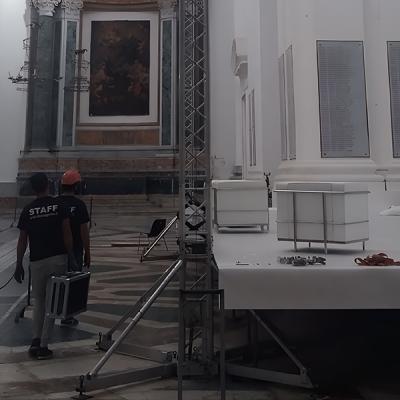 Tecnici allestiscono palco con struttura scenotecnica all'interno di una chiesa storica