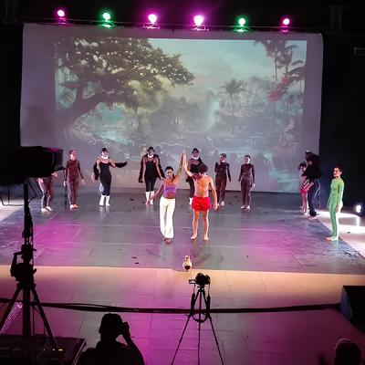 Spettacolo teatrale con ballerini in costume sul palco davanti a scenografia tropicale proiettata