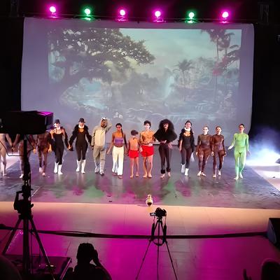 Saluto finale di gruppo di ballerini in costume su palco teatrale con sfondo proiettato di giungla