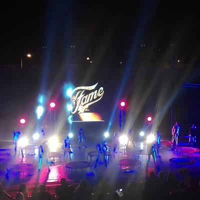 Spettacolo di danza notturno con luci colorate e trampolini, scritta “Fame” su schermo LED