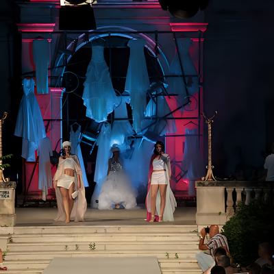 Sfilata di moda serale con modelle in abiti bianchi su passerella scenografica
