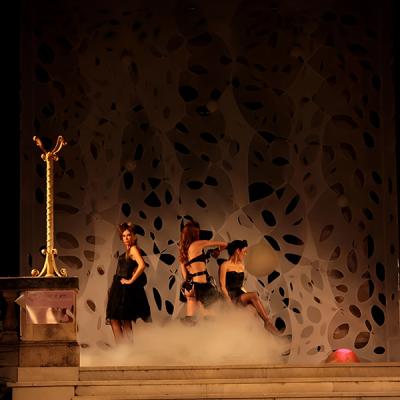 Modelle in abiti neri su passerella con effetti di fumo e sfondo artistico