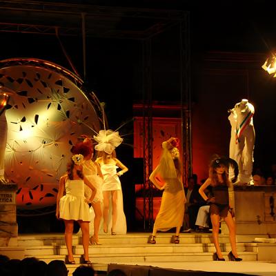 Modelle in abiti da passerella con cappelli scenografici durante una sfilata serale all’aperto