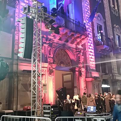 Persone all’ingresso di un edificio storico illuminato con luci scenografiche durante un evento serale