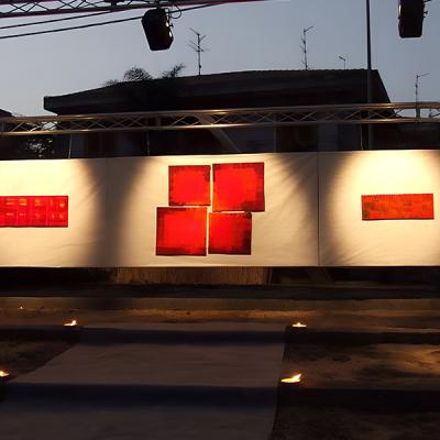 Esposizione serale all’aperto con opere d’arte astratta di colore rosso su pannelli bianchi illuminati da faretti