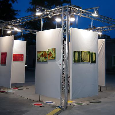 Allestimento serale all’aperto di una mostra d’arte moderna con pannelli bianchi sospesi e dipinti colorati