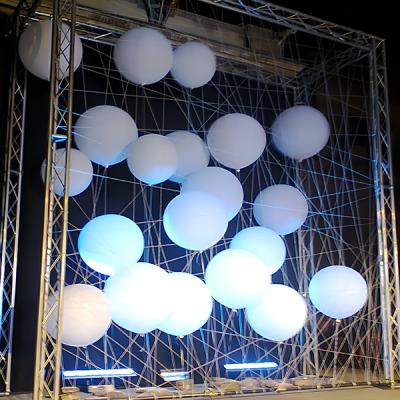 Installazione scenografica notturna con sfere luminose sospese in una struttura metallica intrecciata di corde.