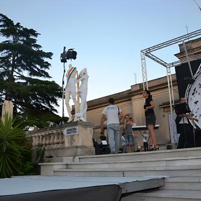 Allestimento scenico all’aperto con struttura in traliccio, scalinata e statue coperte da drappi bianchi, preparazione tecnica di un evento.