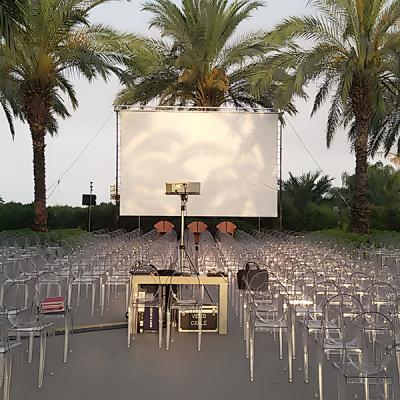 Schermo per proiezioni all'aperto tra palme e sedie trasparenti